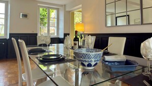 Een eetgedeelte met een glazen tafel, witte stoelen, een blauw-witte kom en een fles wijn.