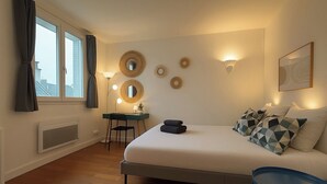 Ein Schlafzimmer mit Bett, Schreibtisch, Stuhl, Heizkörper und einem Fenster mit Vorhängen.