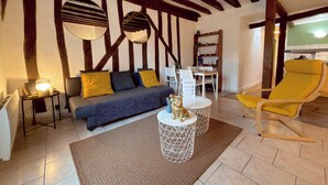 Ein Zimmer mit einer Couch, einem gelben Sessel, einem Esstisch und einem weißen Bücherregal.