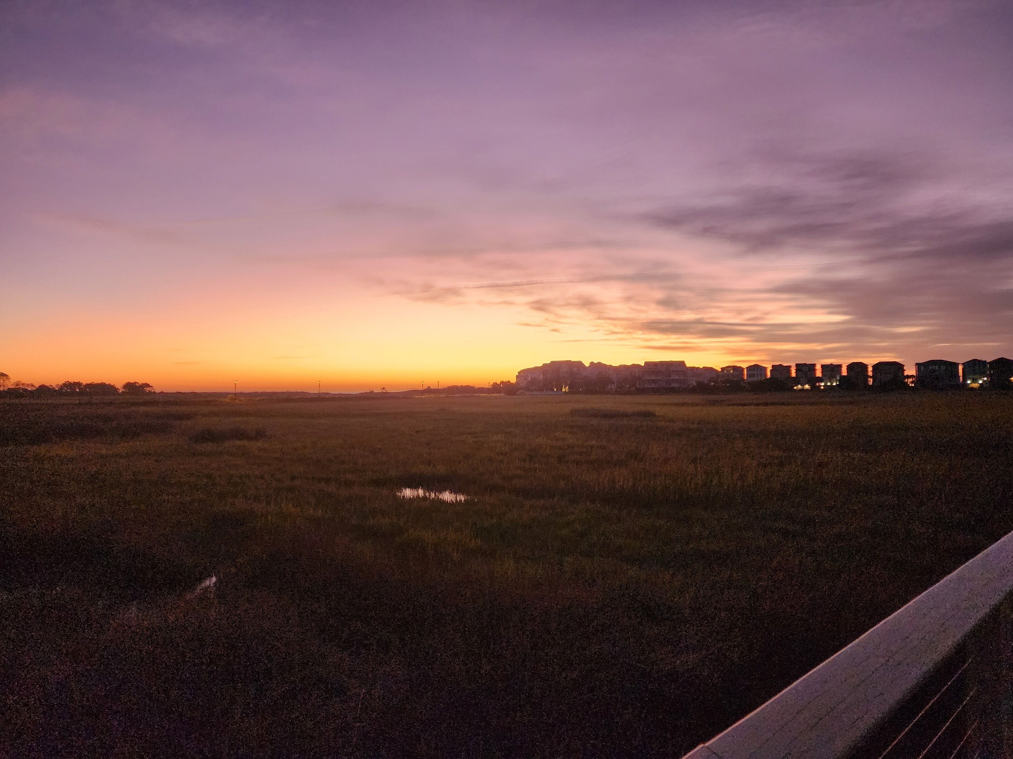 Een zonsondergang boven een vlak landschap met gebouwen in de verte.