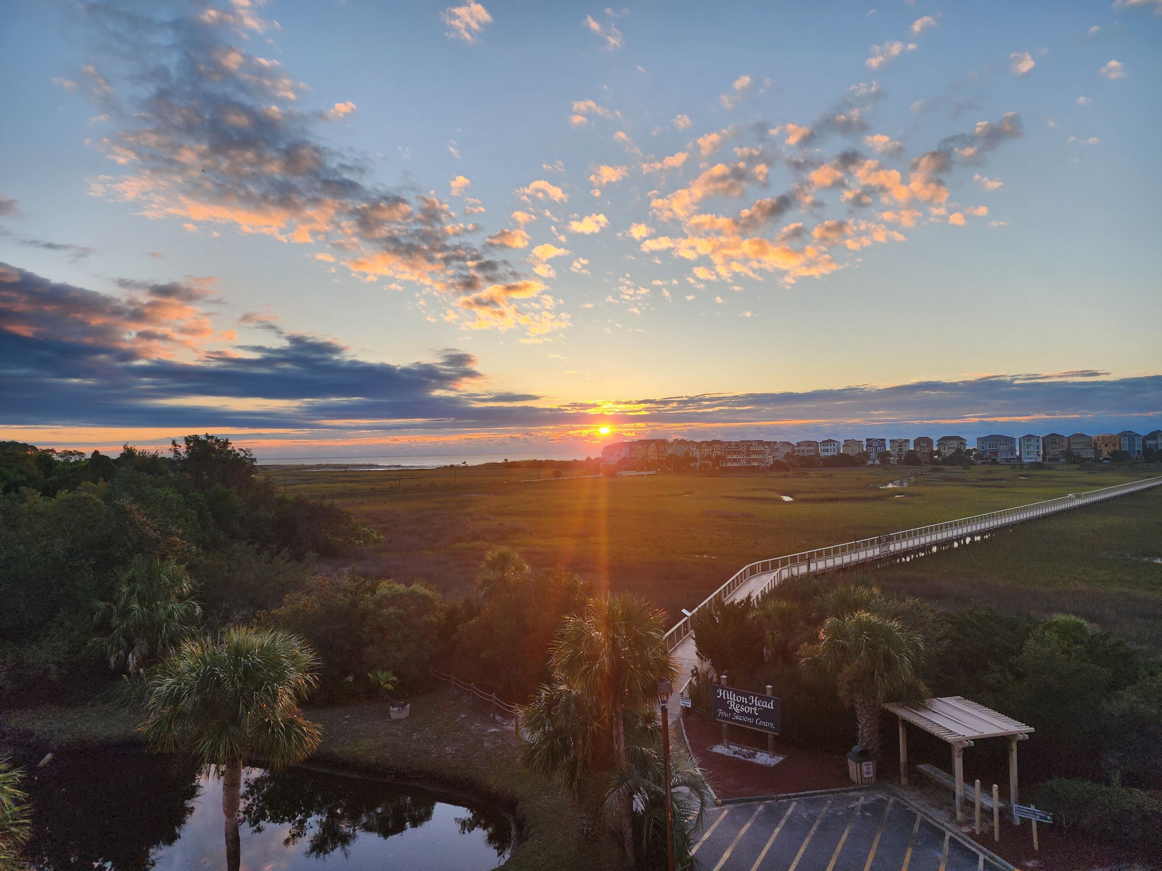 Vista do pôr do sol sobre uma área costeira com uma ponte, palmeiras e uma placa para o Hilton Head Resort.