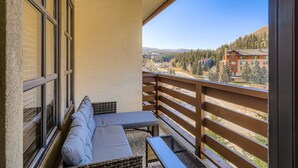 Un balcon aménagé avec un canapé et une table, offrant une vue sur un paysage montagneux et des bâtiments.