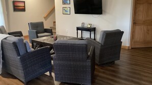 A living room with a TV mounted on the wall, wicker furniture, and a staircase in the background.