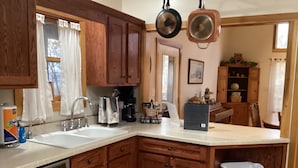 A kitchen with wooden cabinets, a sink, a coffee maker, and a trash can.