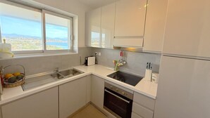 A modern kitchen with white cabinets, a black stove, and a window offering a city view. - 06DJ - Apartment with sea view for 4 people - terrace (Villeneuve-Loubet)
