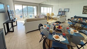 A modern living room with a dining area, large windows, and a view of a cruise ship. - 06DJ - Apartment with sea view for 4 people - terrace (Villeneuve-Loubet)