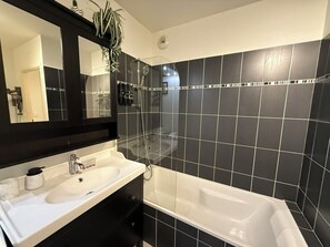 A modern bathroom with a white sink, black cabinets, a large mirror, and a black-tiled shower area. - Cozy apartment in the heart of Nice (Nice)