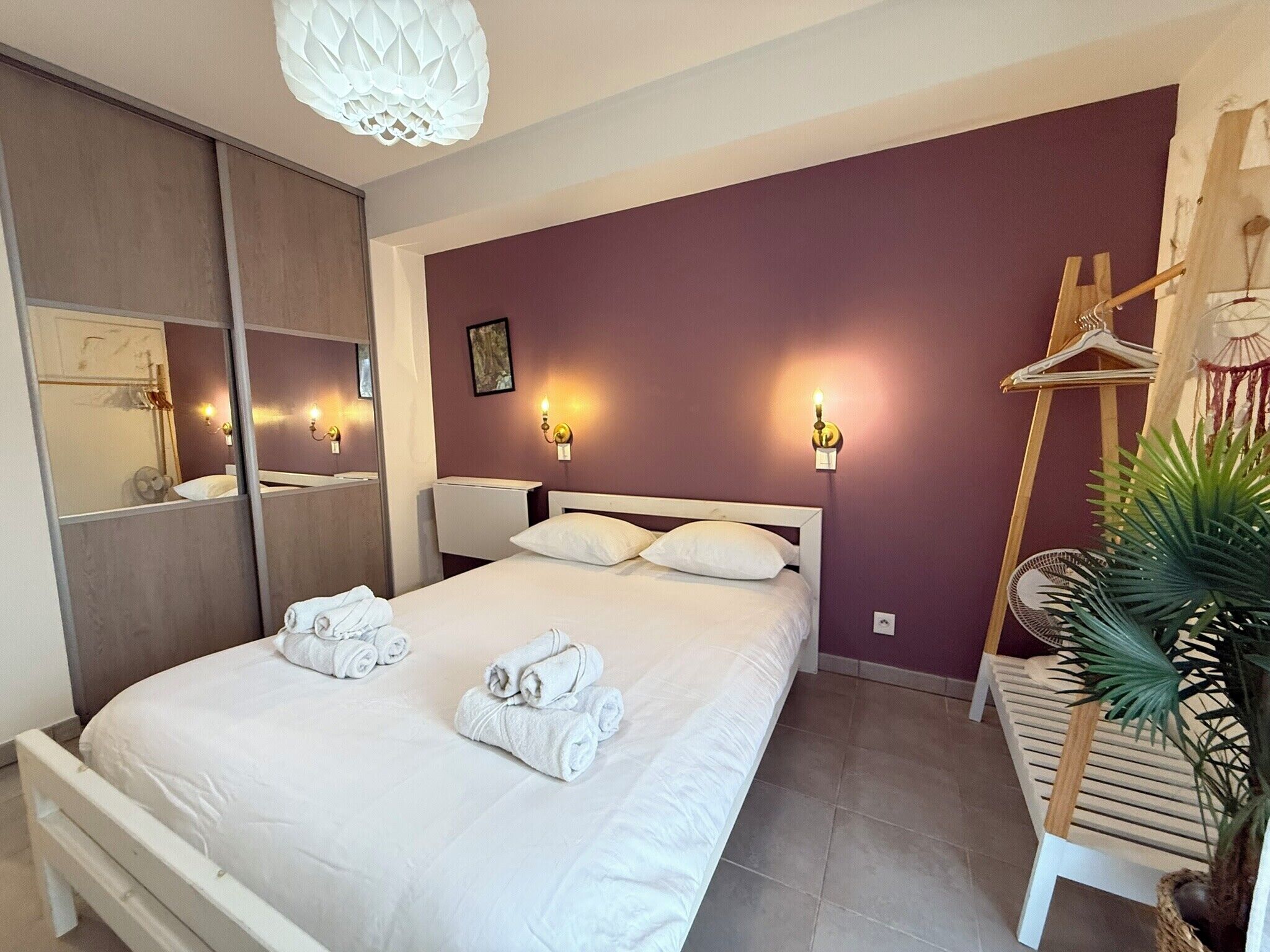 Un dormitorio con cama, un espejo, luces en la pared, una silla de madera y una planta.