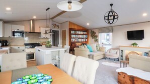 Una cocina moderna con armarios blancos, un comedor con mesa de madera y una sala de estar con sofá y chimenea.