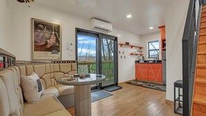 Een moderne woonkamer met een beige bank, een glazen salontafel en een Star Wars poster. Er is een schuifpui die uitkomt op een balkon met groene stoelen.
