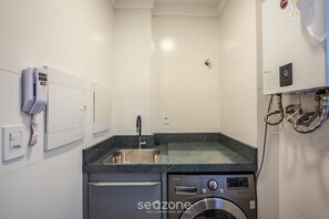 A compact kitchen with a built-in washing machine, a sink, and a telephone. - Apt w/ Barbecue Grill 850 m From the Beach Sem0302 (Itapema)