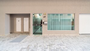 Entrada d'un edifici amb una porta de vidre, un senyal amb el número 90 i una finestra amb persianes.