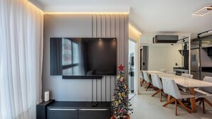 Un saló modern amb televisió de pantalla plana, un petit arbre de Nadal i zona de menjador amb taula llarga i cadires.