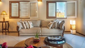 Een woonkamer met een beige bank, een ronde salontafel en een lamp.