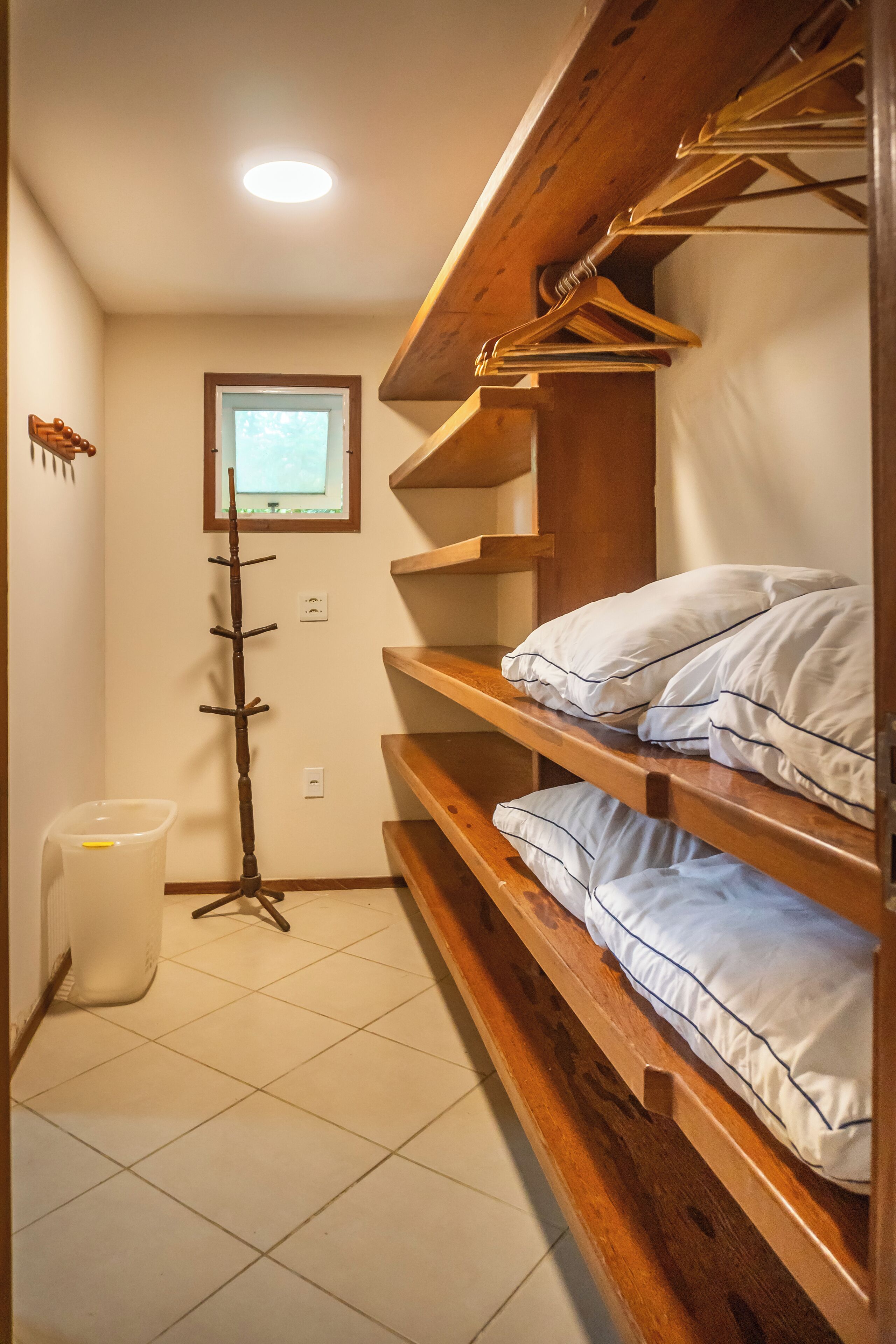 Ein kleines Zimmer mit Etagenbetten, einem Kleiderhaken, einem Fenster und einem Mülleimer.