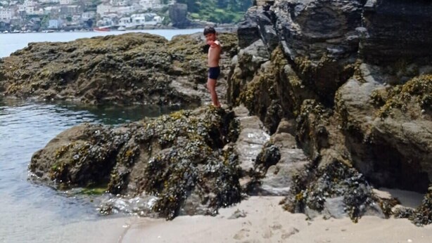 En stenet strand med en person stående på klipperne.