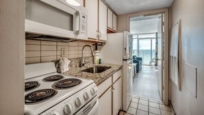 Eine kleine Küche mit Herd, Spüle und Mikrowelle. Durch eine geöffnete Tür ist ein Balkon zu sehen.