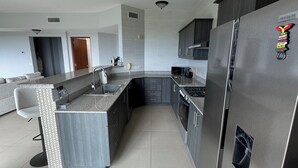 Eine moderne Küche mit grauen Schränken, einem Edelstahlkühlschrank und einer grauen Kücheninsel mit Barhocker.