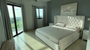 Ein geräumiges Schlafzimmer mit einem großen Bett, einem Deckenventilator, Blick ins Freie und einer hölzernen Bank.