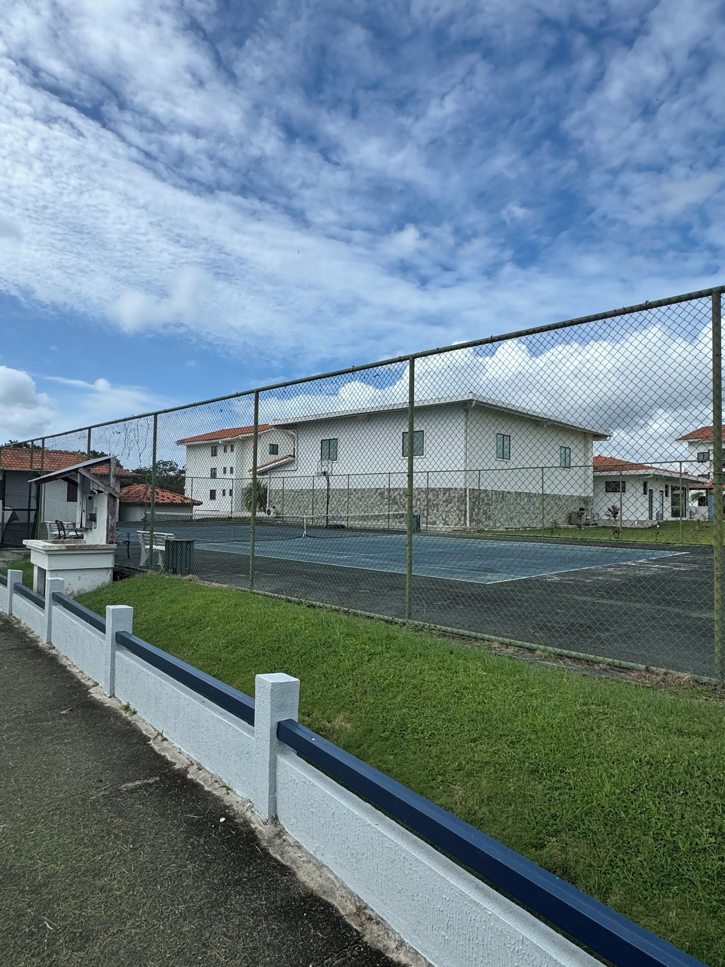 Ein eingezäunter Tennisplatz mit einem Gebäude im Hintergrund.