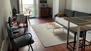 Ett vardagsrum med en soffa, ett matbord, stolar, ett skåp och en utsikt genom en glasdörr ut mot ett utomhusområde.