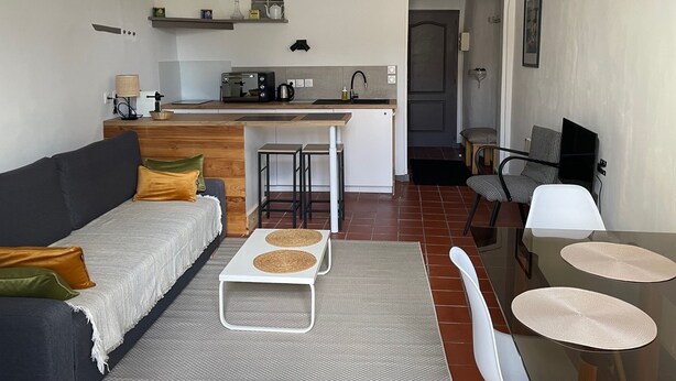 Ett kompakt bostadsutrymme med ett litet kök, en soffa, ett matbord och en stol.