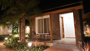 A modern outdoor patio with a stone wall, a wooden pergola, and a table with chairs. - KUSUM RESORT (Badami)