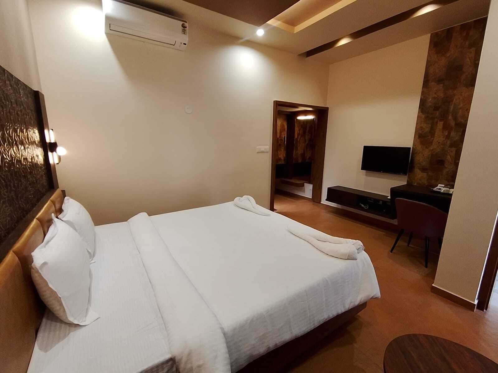 A modern hotel room with a large bed, a flat-screen TV, a desk, and a seating area.
