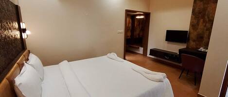 A modern hotel room with a large bed, a flat-screen TV, a desk, and a seating area.