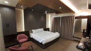 A modern hotel room with a large bed, a desk with a coffee maker, a chair, and a wardrobe. - KUSUM RESORT (Badami)