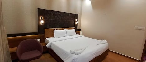 A hotel room with a bed, a chair, a small table, a ceiling fan, and an air conditioning unit.