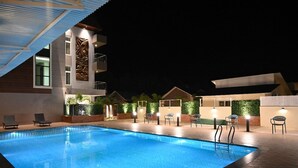 A swimming pool with lounge chairs and a modern building with balconies. - KUSUM RESORT (Badami)