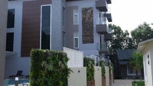 A modern building with a flat roof, a balcony, and a pathway leading to a door. - KUSUM RESORT (Badami)