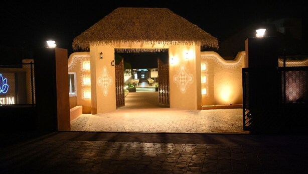A building with a thatched roof entrance, illuminated by warm lights, leading to a well-lit interior. - KUSUM RESORT (Badami)
