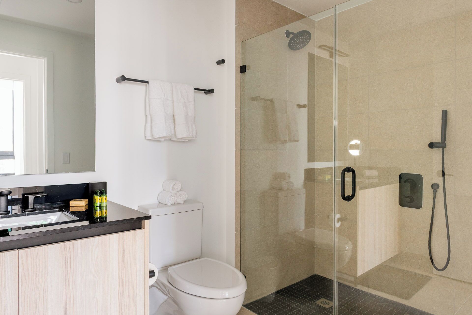 A modern bathroom with a glass-enclosed shower, a toilet, and a sink with a black countertop.