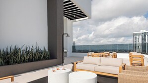 A rooftop terrace with a sofa, two round tables, and wicker chairs. - District 225 by Nomada (Miami)