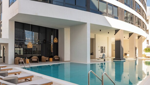 A modern hotel pool area with lounge chairs, a clear pool, and a view of the city skyline. - District 225 by Nomada (Miami)