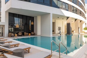 Ein moderner Hotelpoolbereich mit Liegestühlen, klarem Wasser und Blick auf die Skyline der Stadt.