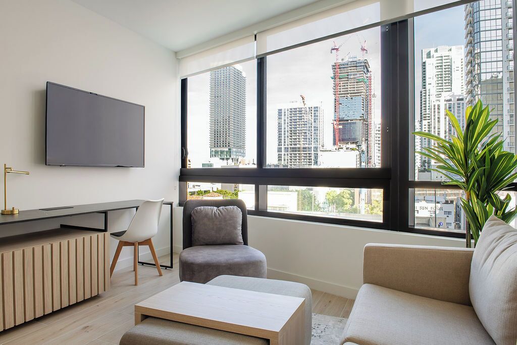 A modern living room with a large window, a flat-screen TV, a sofa, a chair, and a coffee table.