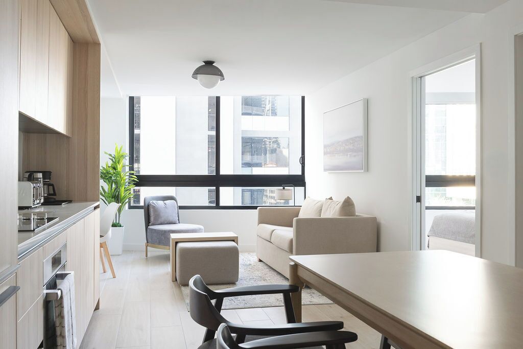 Un apartamento moderno con cocina, comedor y sala de estar. Cuenta con ventanas amplias, una lámpara de techo y vistas a la ciudad.