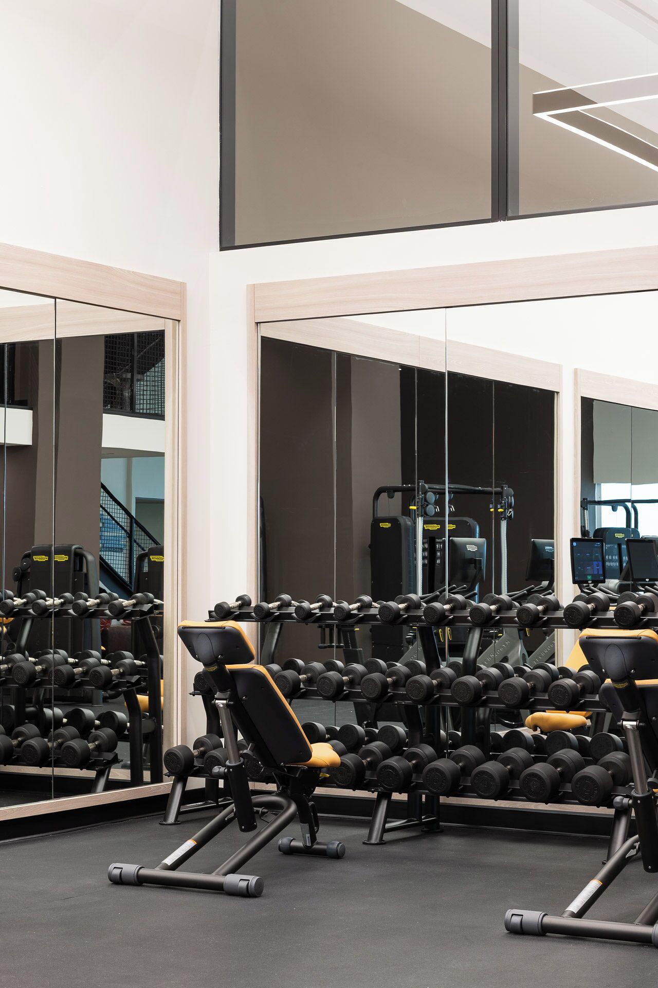 A gym with multiple dumbbell racks, exercise machines, and mirrors on the walls.