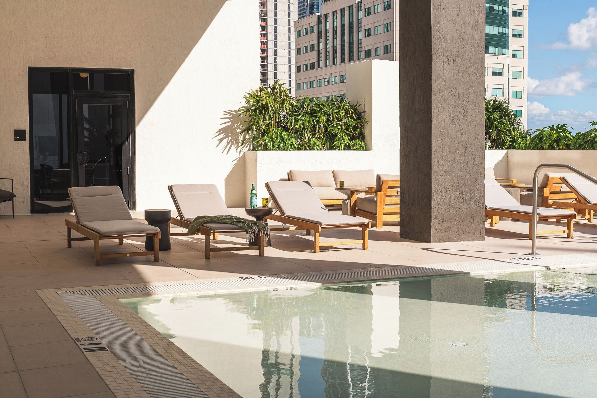A rooftop pool area with lounge chairs and a small table, surrounded by a high-rise building.