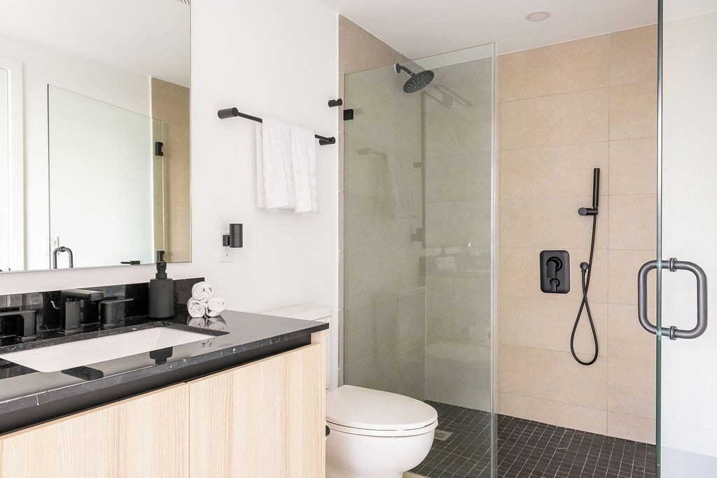 A modern bathroom with a glass-enclosed shower, a white toilet, and a black countertop sink.