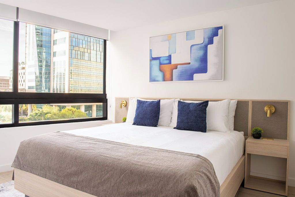 Una habitación de hotel moderna con una cama grande, vistas a la ciudad y un cuadro abstracto contemporáneo en la pared.