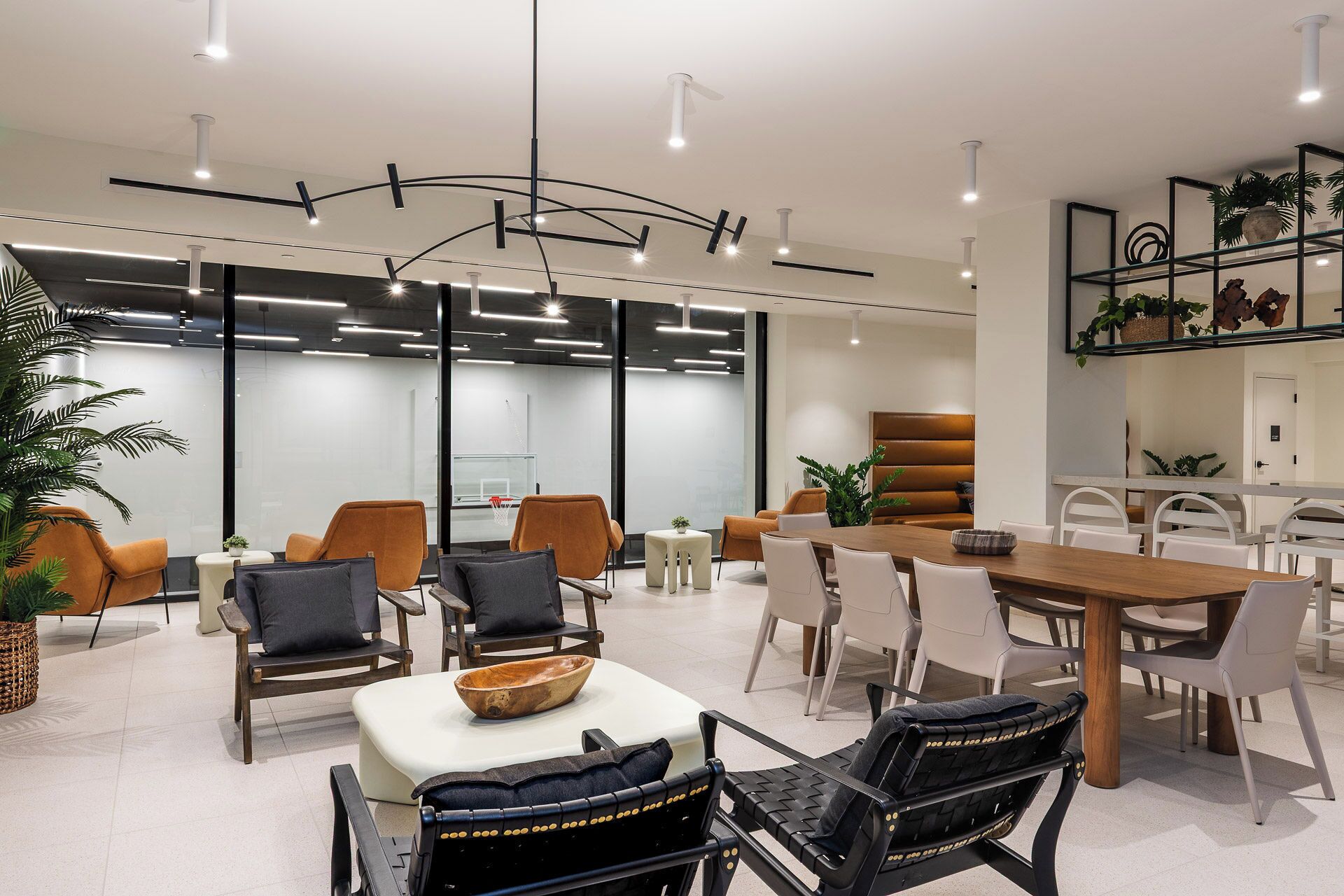 Un espace repas moderne avec une longue table en bois, plusieurs chaises et une table blanche au centre.