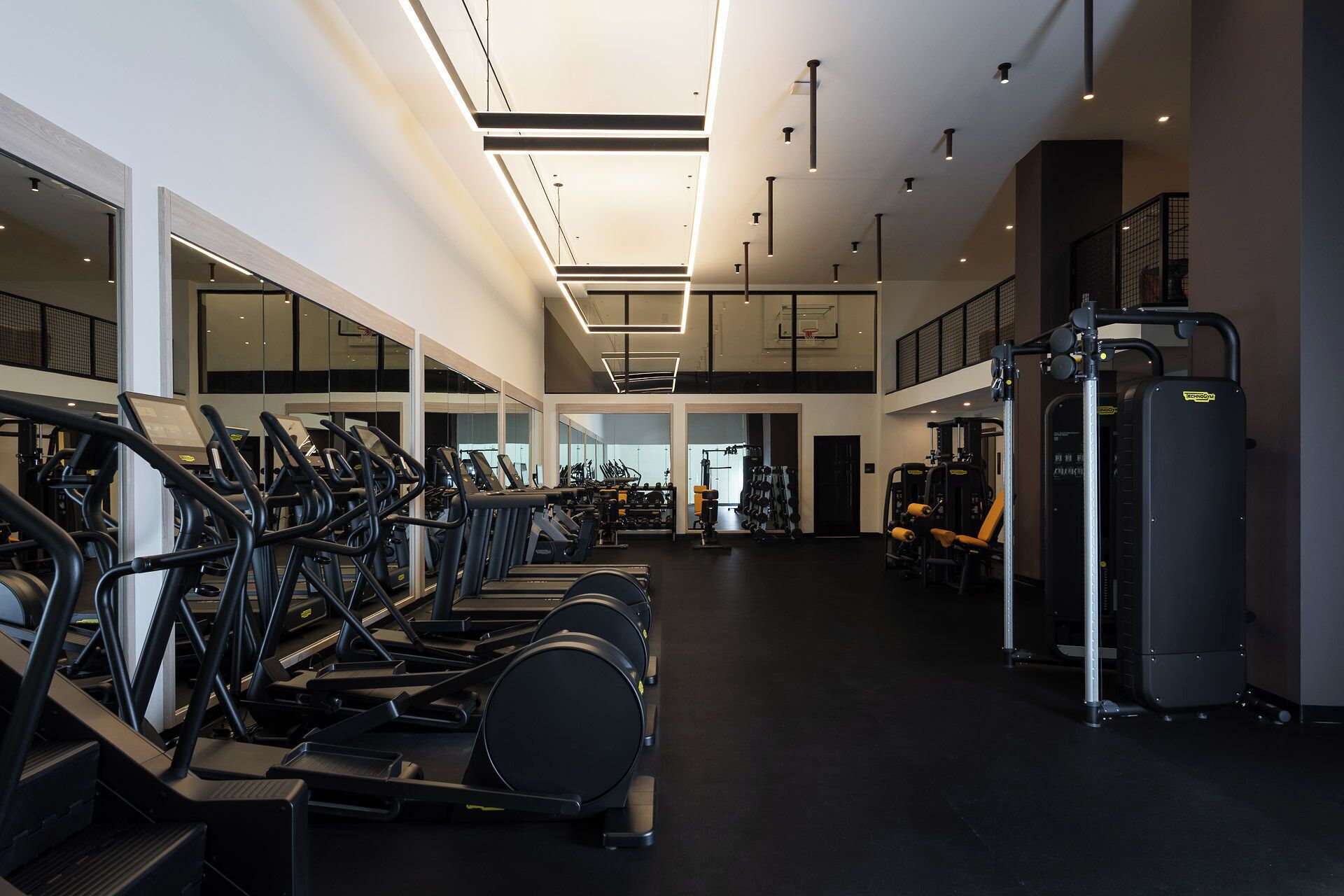 A spacious gym with multiple treadmills, weight machines, and a basketball court.