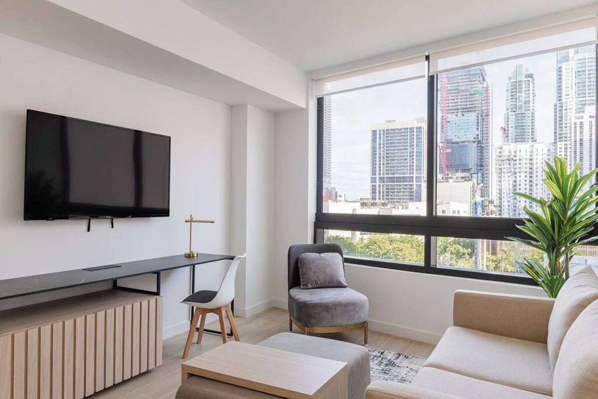 Ein modernes Wohnzimmer mit Flachbildfernseher, Essbereich und großem Fenster mit Blick auf die Stadt.
