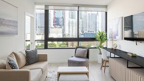 A modern living room with a large window, a sofa, a coffee table, a TV, and a plant. - District 225 by Nomada (Miami)