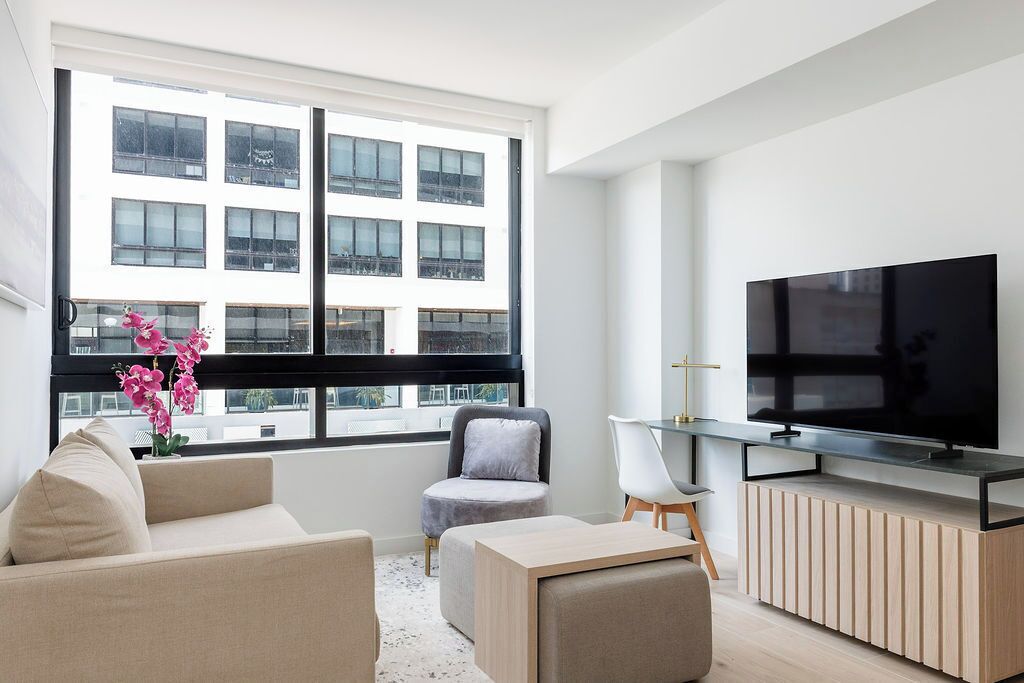 Ein modernes Wohnzimmer mit großem Fenster, einem Flachbildfernseher, einer Couch, einem Sessel und einem kleinen Tisch.