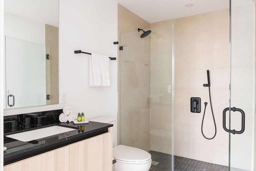 Une salle de bain moderne avec une douche à parois de verre, des toilettes blanches et un plan de toilette noir avec un lavabo.
